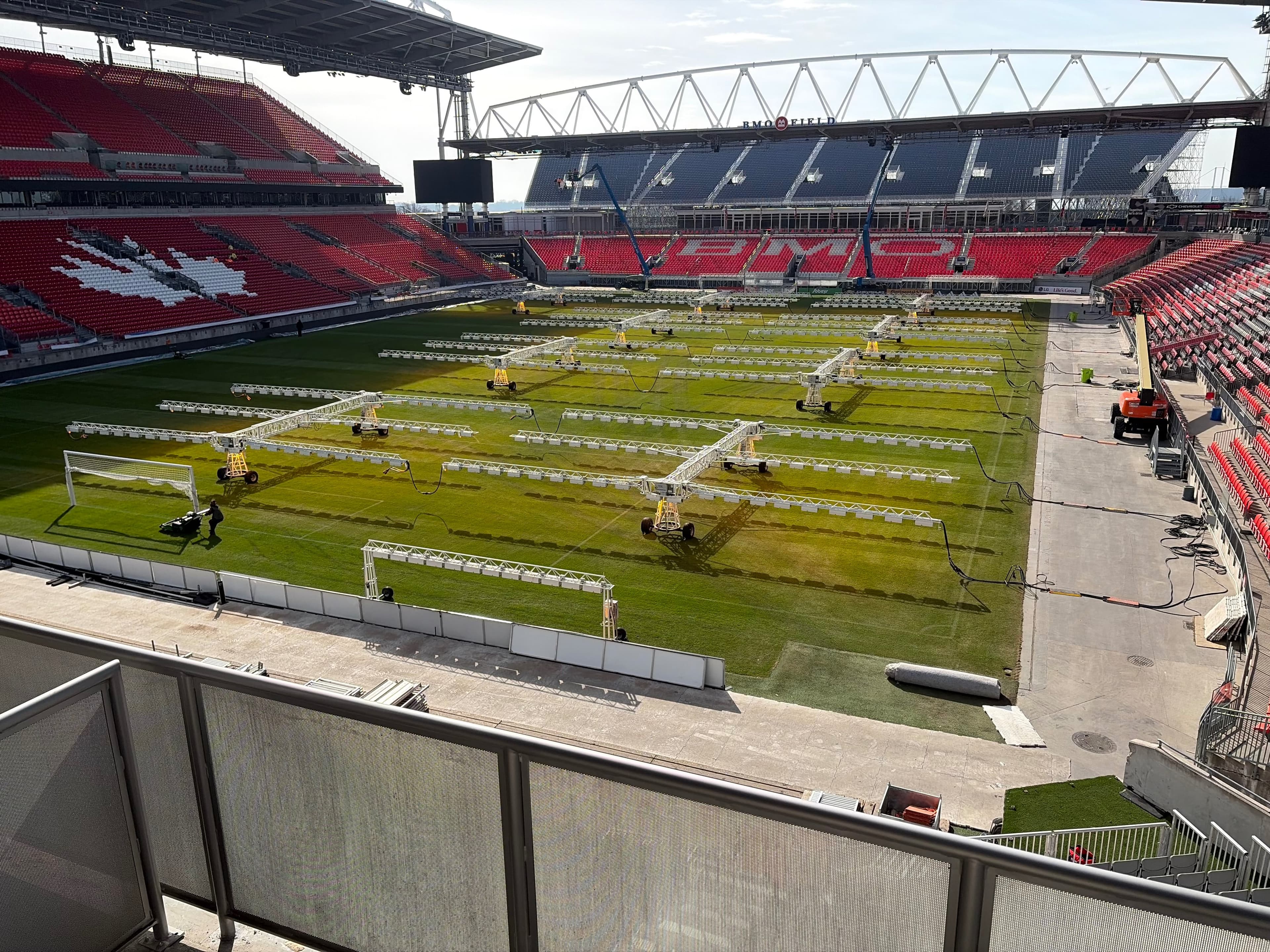 Finished perforated metal guard railing in the foreground overlooking the BMO Field pitch, with red stadium seating spelling BMO and a maple leaf