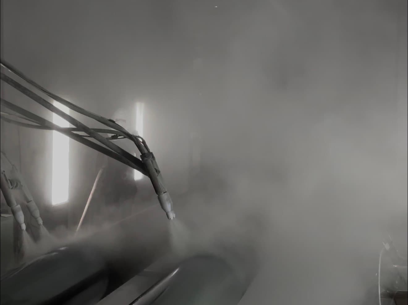 Bank of automatic powder guns on articulated mounts spraying a cloud of grey powder onto steel pipe sections in PPC's booth
